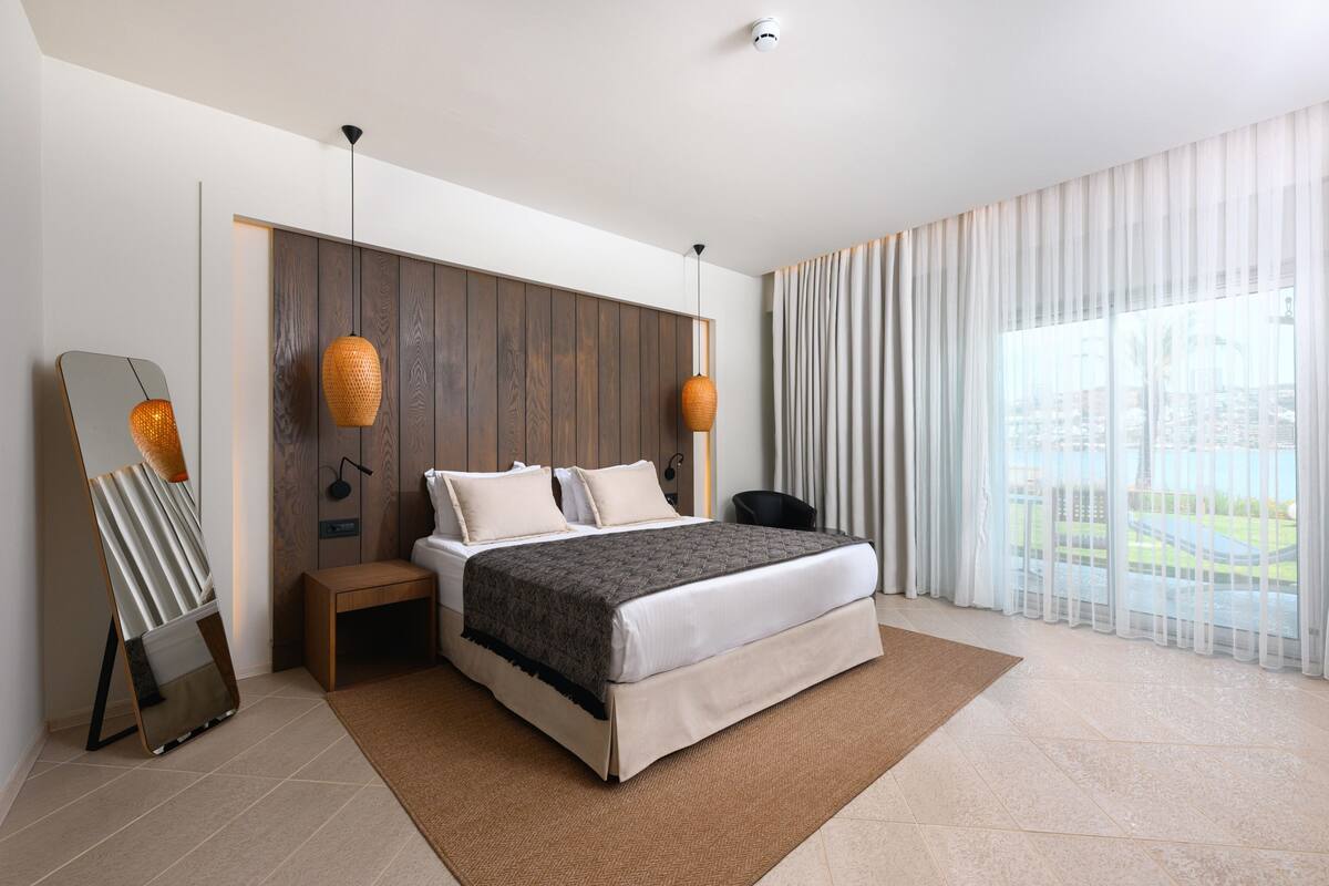 Een moderne slaapkamer met een bed, nachtkastjes, een spiegel en uitzicht op het natuurlijke landschap.