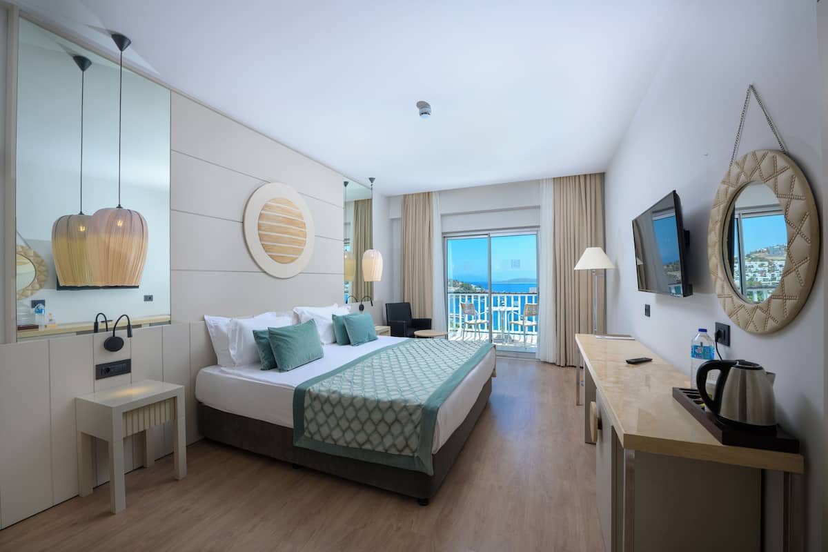 Een hotelkamer met een bed, nachtkastje, bureau en een balkon met uitzicht.