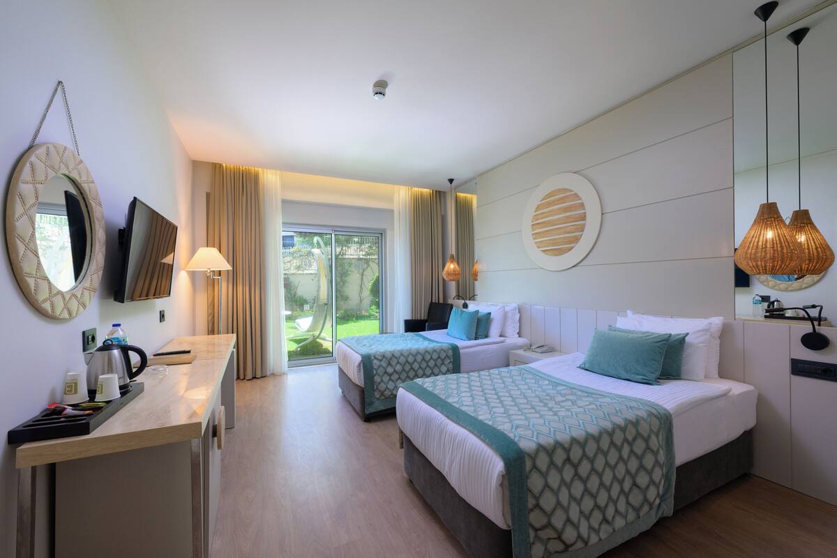 Een hotelkamer met twee bedden, een bureau met waterkoker, een televisie en uitzicht op het groen.