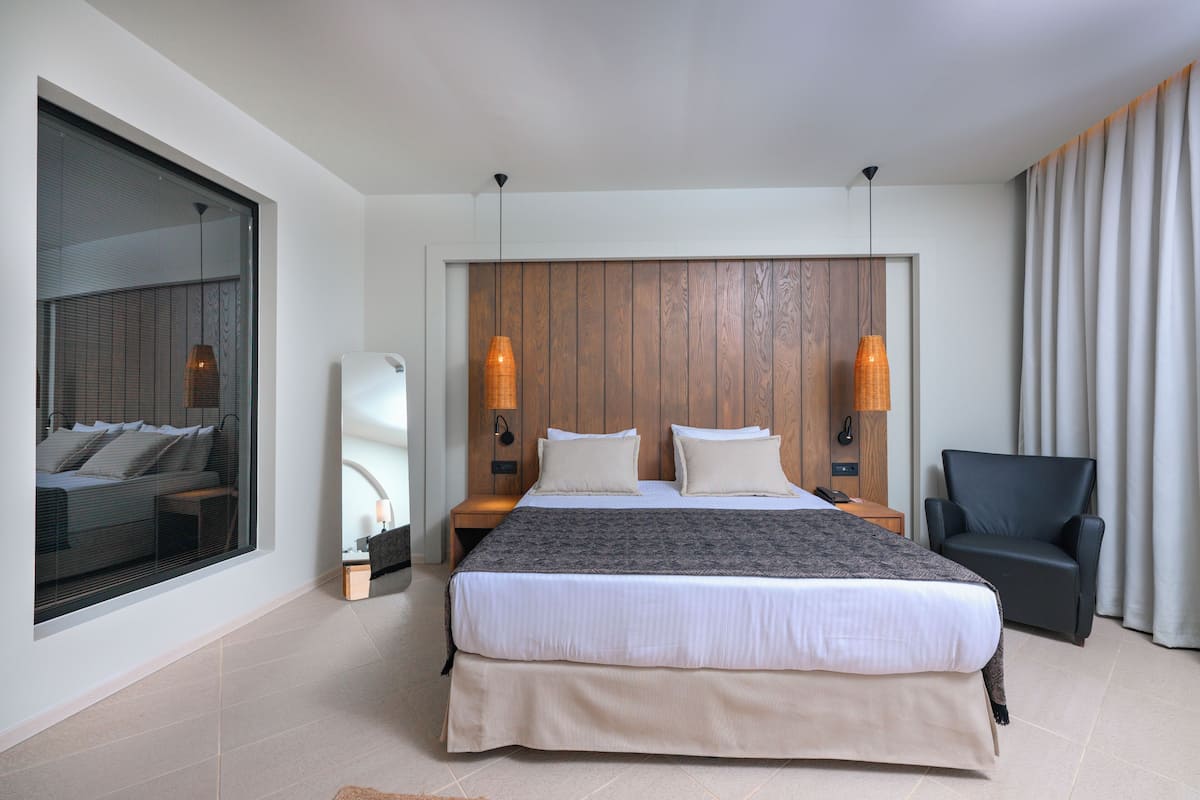 Een moderne hotelkamer met een groot bed, een zithoek met een fauteuil, een groot raam en een houten accentmuur.