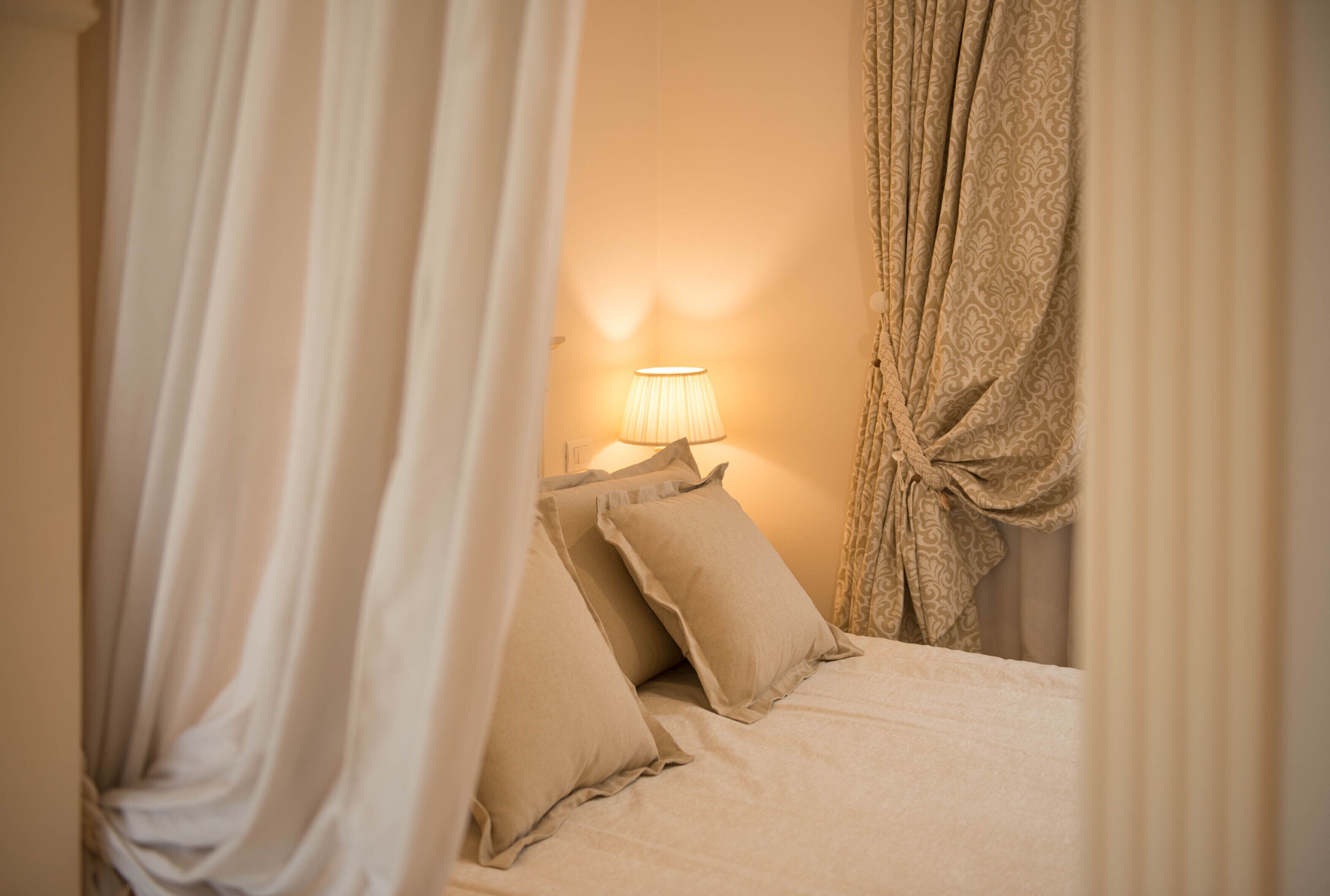 A bedroom with a bed, pillows, a lamp, and curtains.