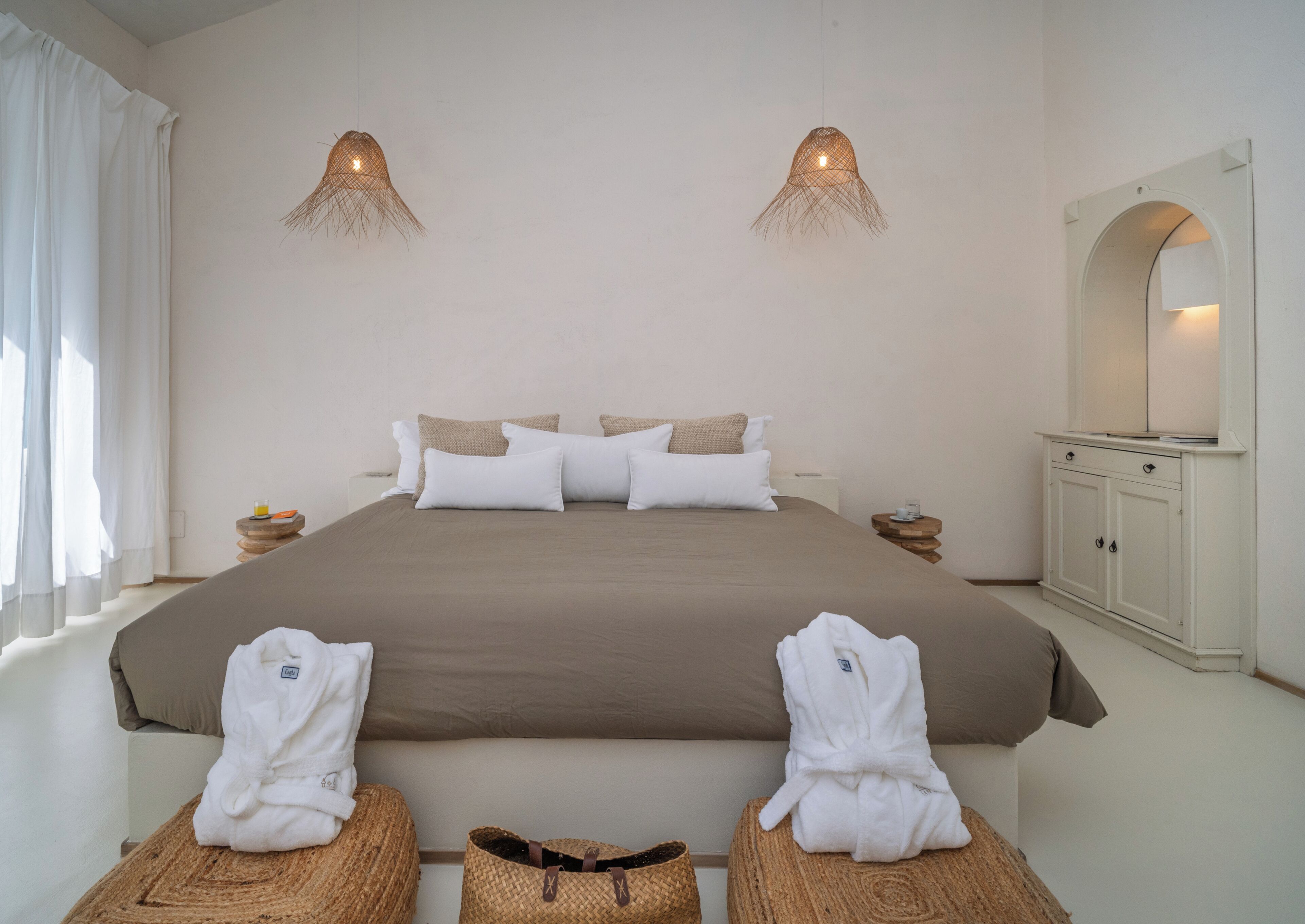 A bedroom with a large bed, two bedside tables, a wardrobe, and two hanging lamps.