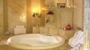 A spa room with a large oval bathtub, a stone wall, a candelabra, and a small fountain.