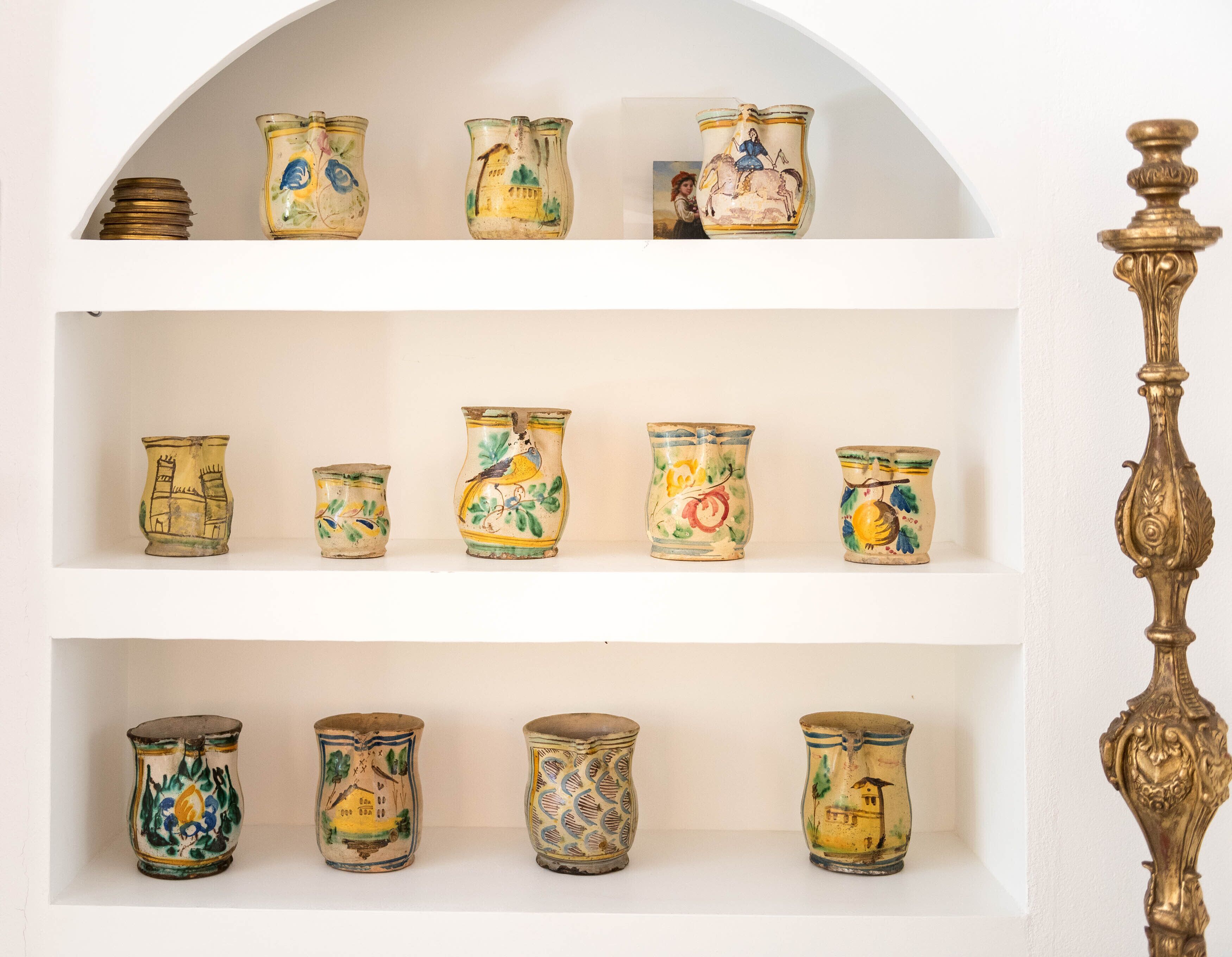 A display of ceramic vases with various designs, arranged on shelves against a white wall.