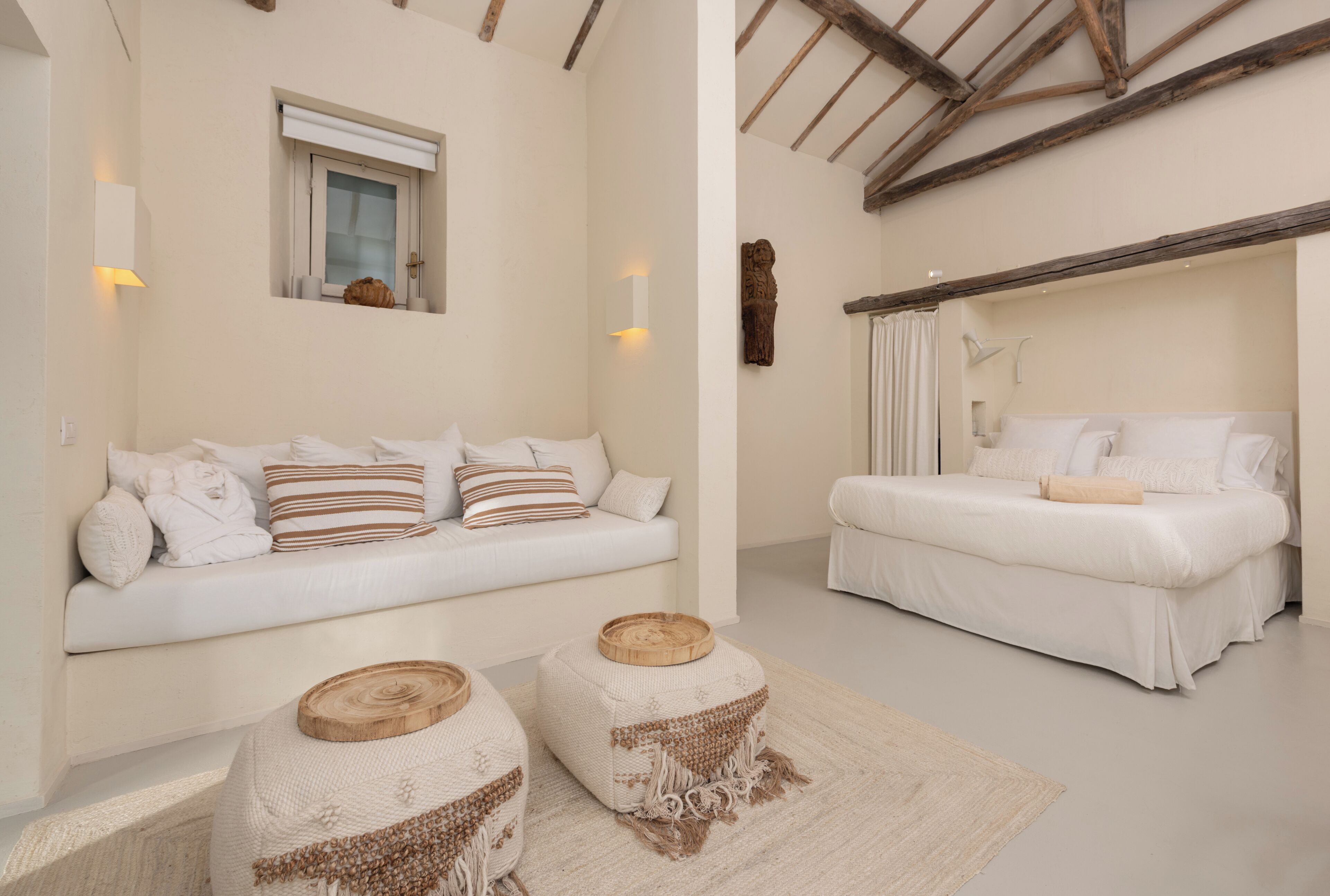 A modern bedroom with a white sofa, a bed, and a wooden accent piece on the floor.
