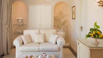 A cozy living room with a white sofa, a glass coffee table with pastries, and a vase with yellow flowers.