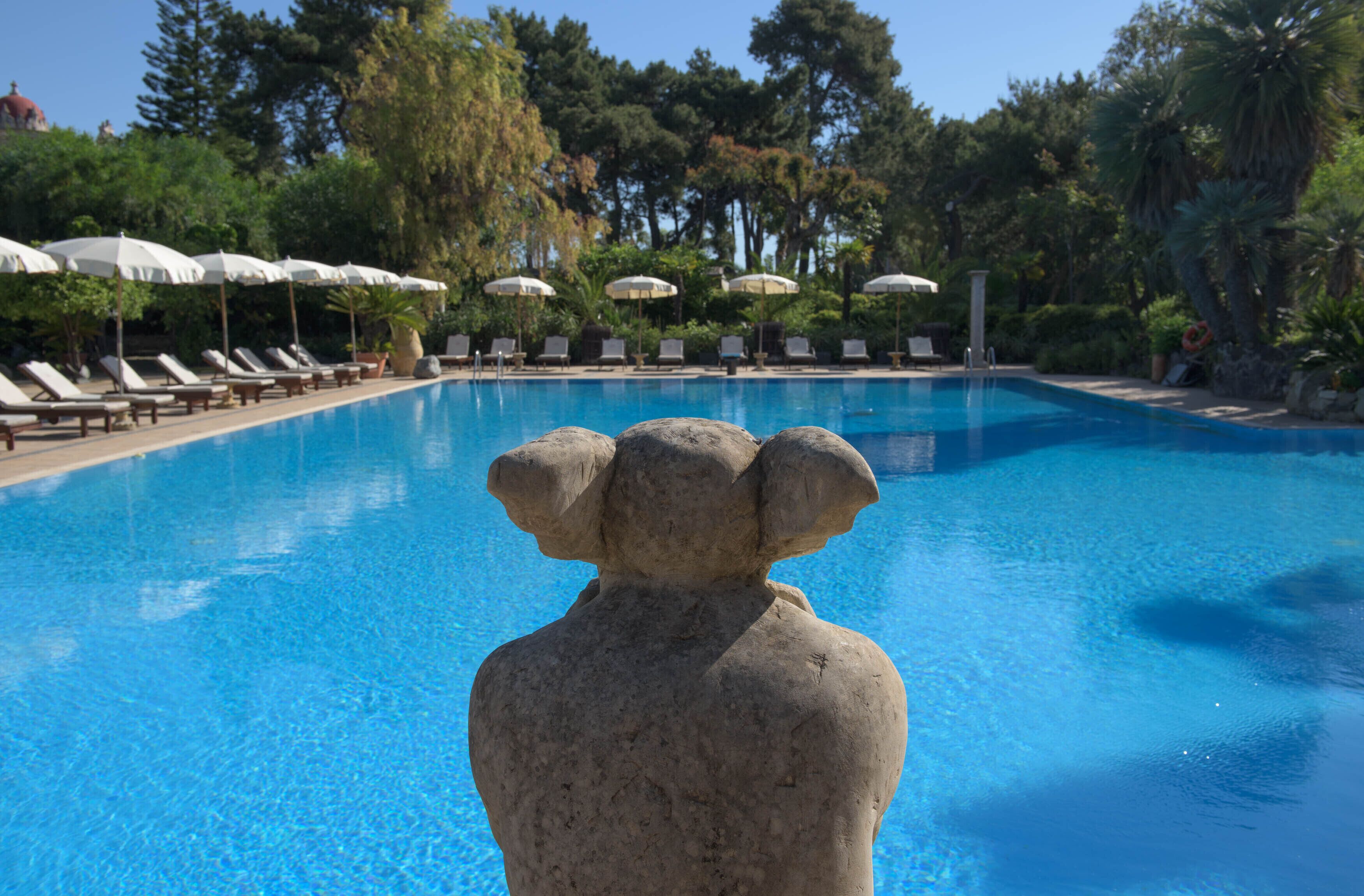 Una piscina con sillas de descanso y sombrillas, rodeada de árboles.