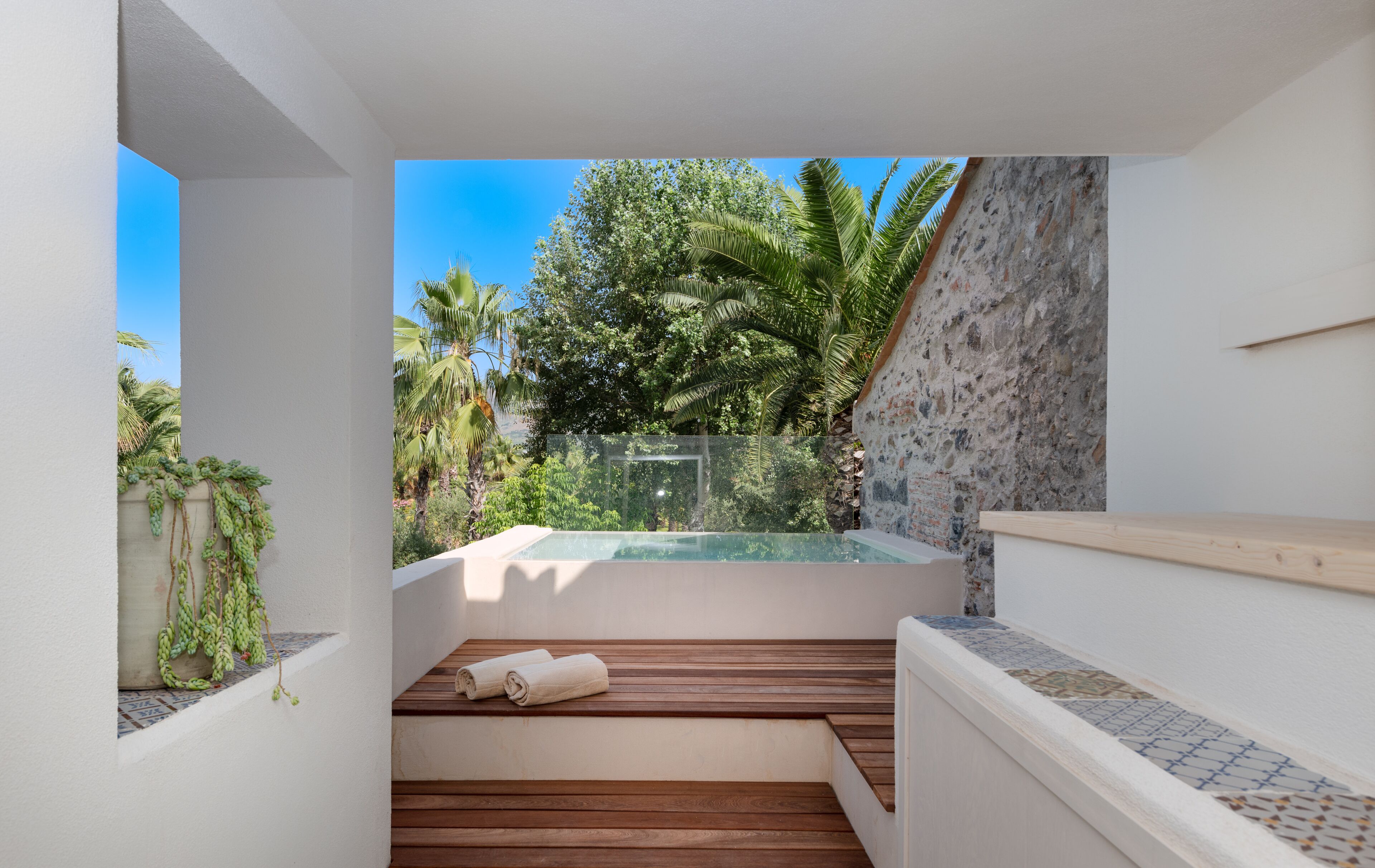 A modern outdoor pool area with a wooden deck and a stone wall.