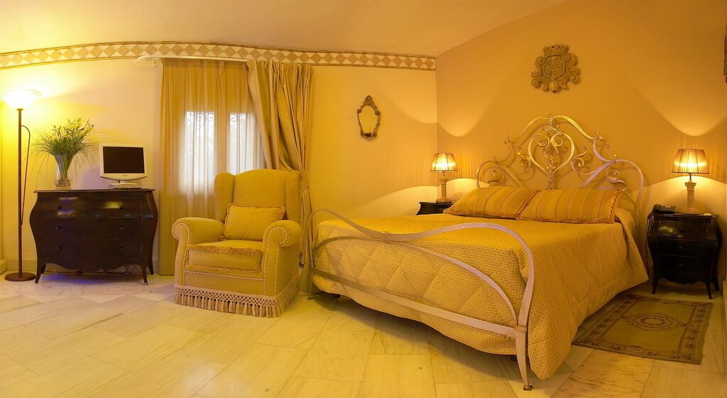 Un dormitorio con cama, dos mesitas de noche, una silla, cómoda, televisor y cortinas.