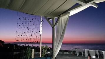 Eine Terrasse direkt am Strand mit Meerblick, einer Netzdekoration und einem weißen Zaun.