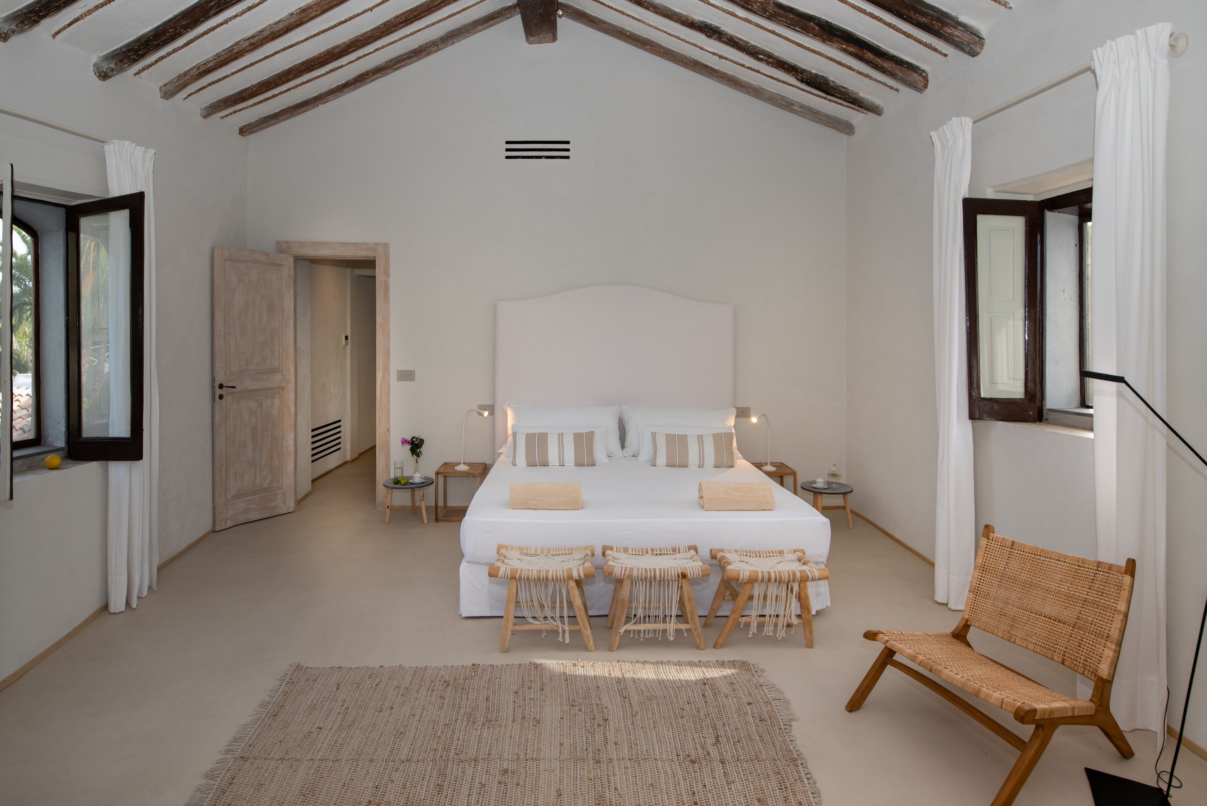 A bedroom with a large bed, bedside tables, a chair, and a view of the outdoors.