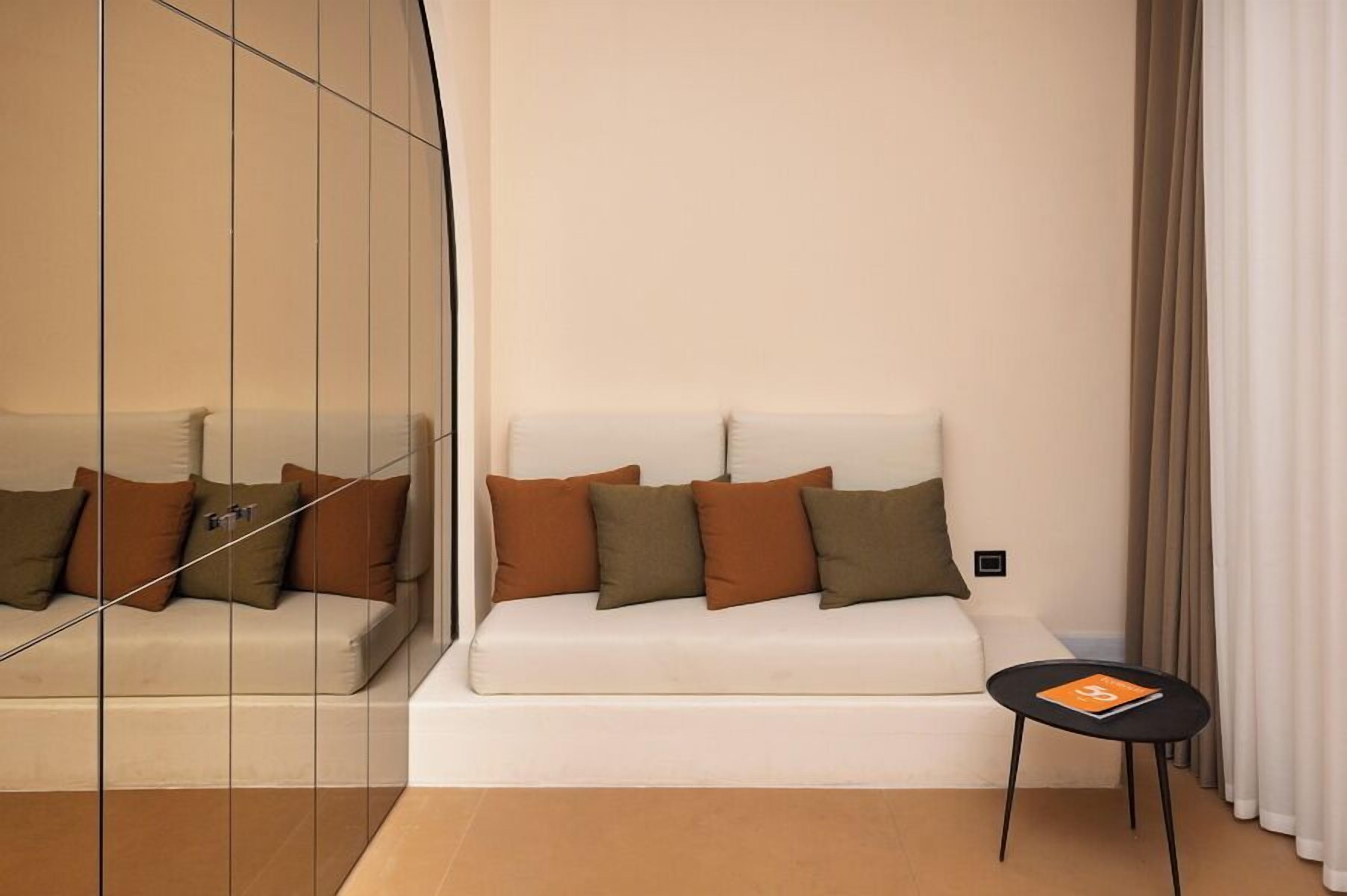 A modern living room with a white sofa, brown cushions, a small black side table, and a glass partition.