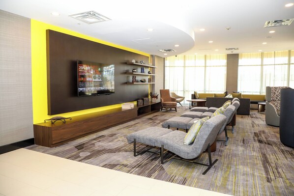Eine moderne Hotellobby mit einem an der Wand befestigten Flachbildfernseher, einer Sofaecke mit verschiedenen Sitzmöglichkeiten und einem gemusterten Teppich.