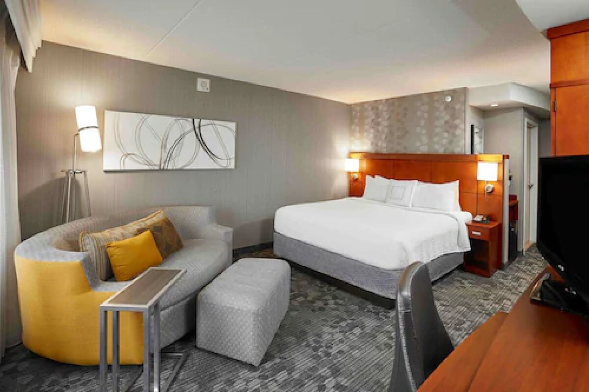 A hotel room with a bed, a sofa, a small table, a TV, and a wall art piece.