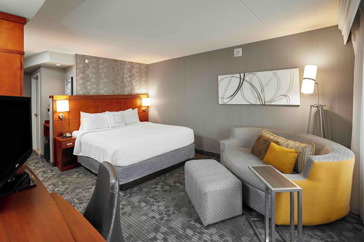 A hotel room with a bed, a sofa, a desk, and a television.