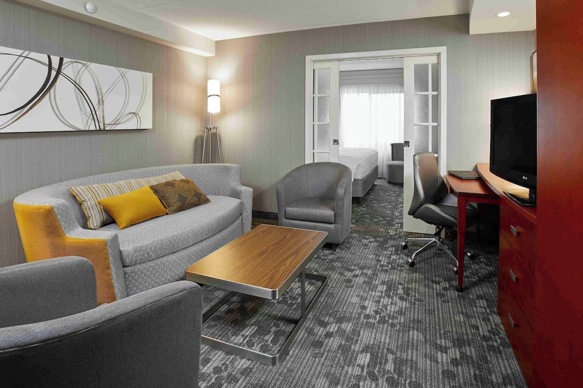 A hotel room with a grey sofa, a wooden coffee table, a TV, and a desk with drawers.