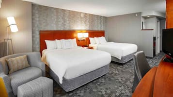 A hotel room with two beds, a desk, a chair, and a TV.