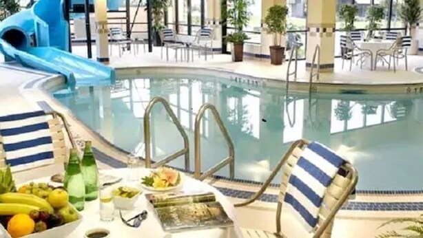 A pool area with lounge chairs, a table with fruit and drinks, and a blue slide. - Courtyard by Marriott Toronto Brampton (Brampton)