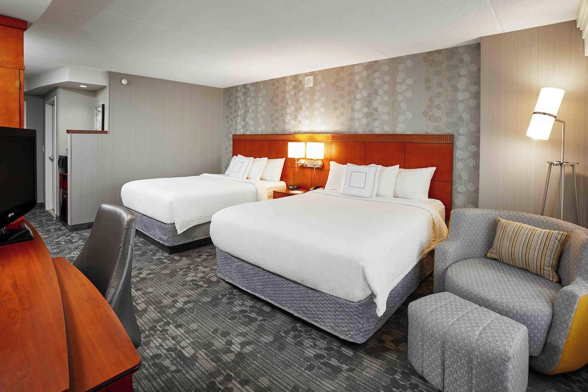 A hotel room with two beds, a desk, a chair, and a sofa.