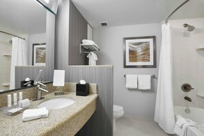 Ein modernes Badezimmer mit Marmorwaschtisch, einem großen Spiegel, einem gerahmten Kunstwerk, einer Toilette und einer Duschkabine.