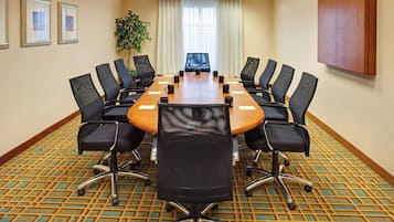 Un salón de conferencias con una gran mesa, sillas negras y una planta.