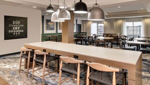 A modern dining area with a long table and bar stools, overhead pendant lighting, and a city view through large windows. - Fairfield Inn and Suites by Marriott Toronto Brampton (Brampton)