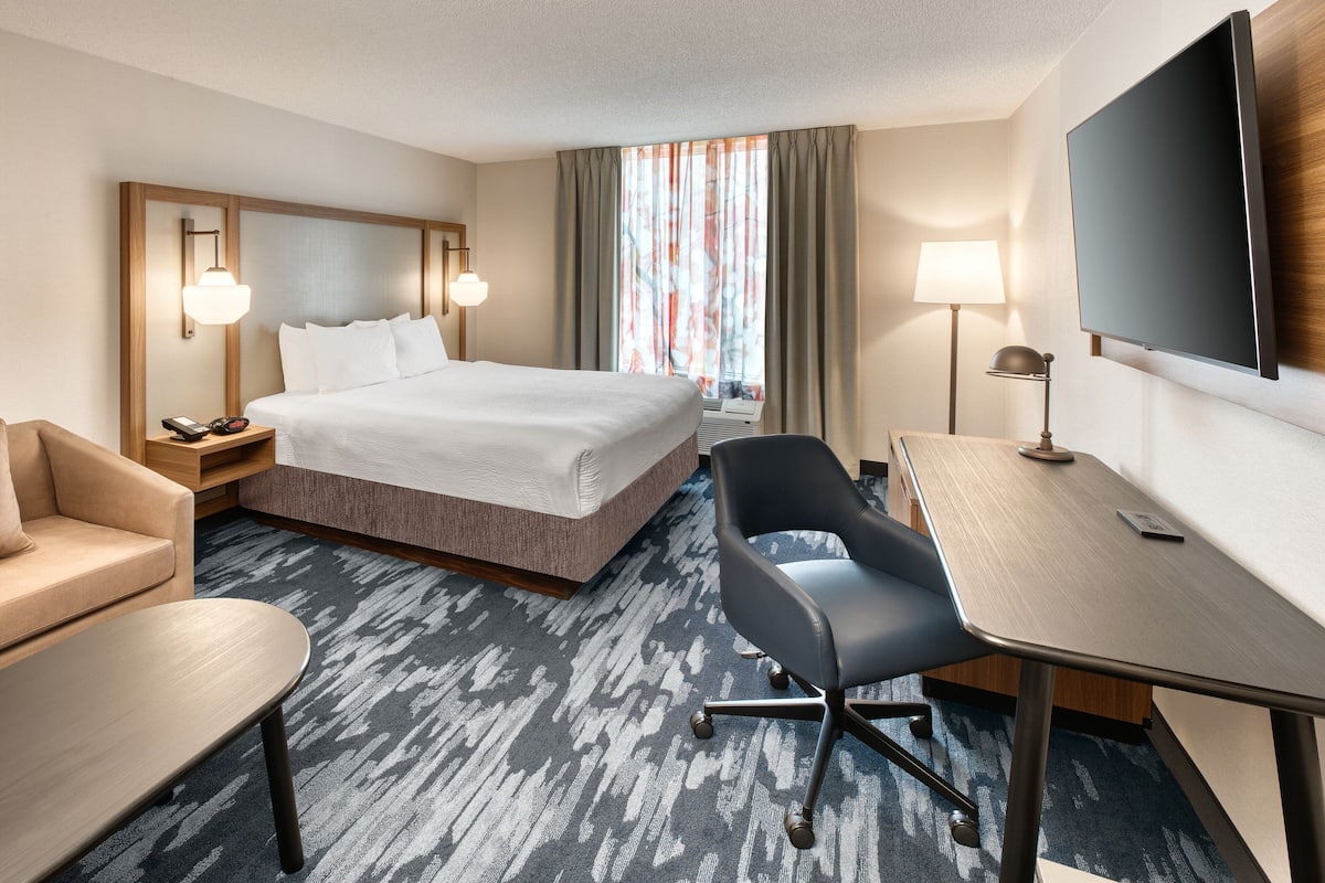 A hotel room with a bed, a desk, a chair, a TV, and a lamp.