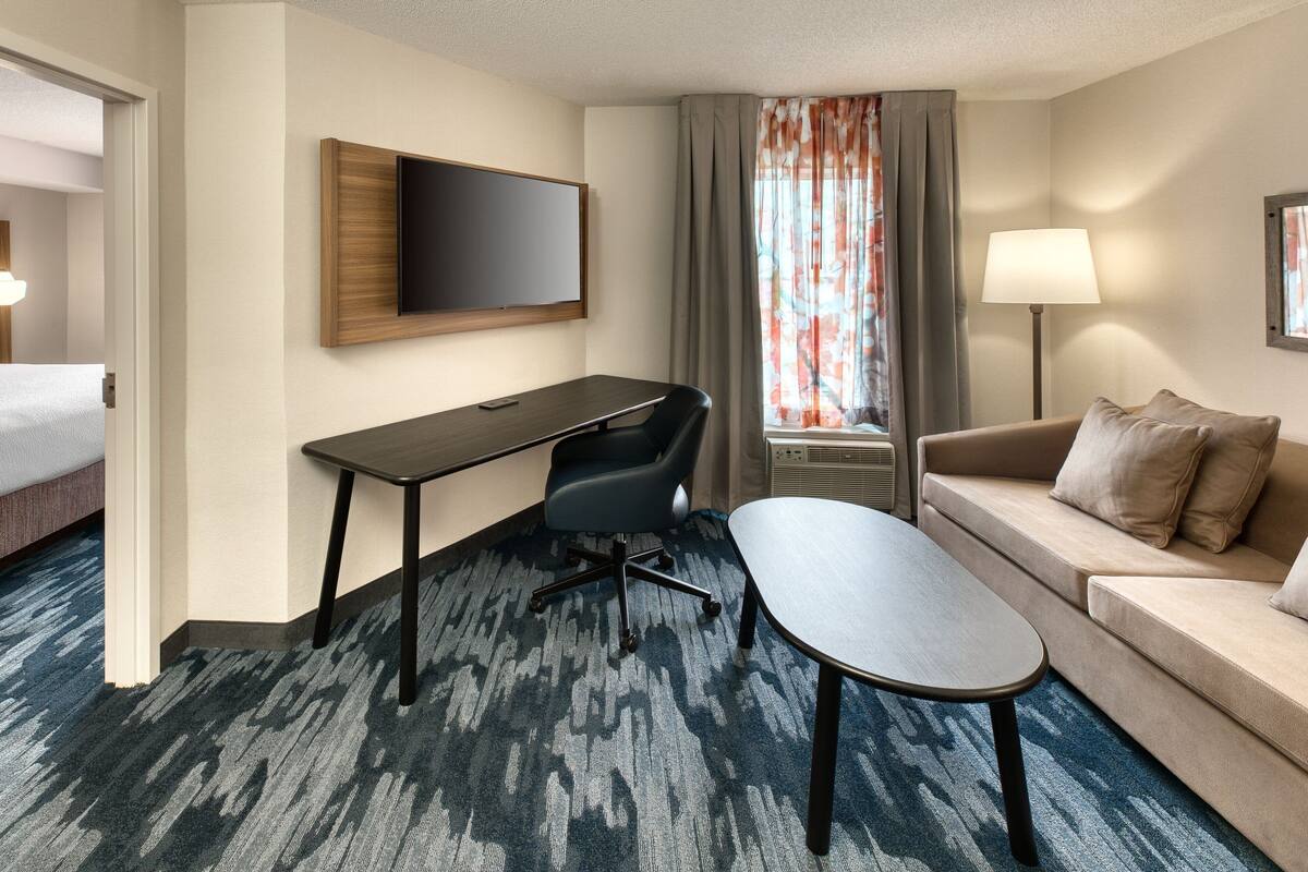 A hotel room with a bed, a desk, a chair, a sofa, a TV, a lamp, and a window with curtains.
