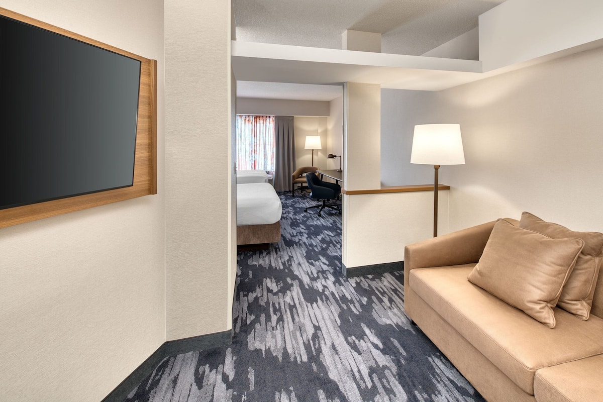 A hotel room with a large bed, a sofa, a desk, and a TV.