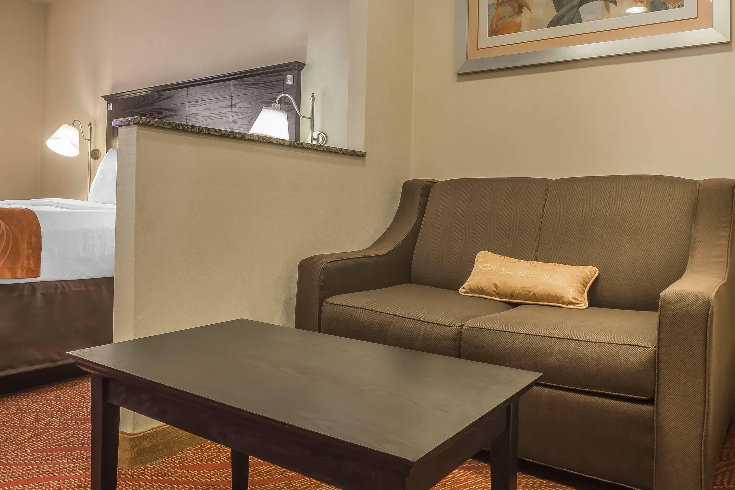 A hotel room with a bed, a brown sofa, a small table, and a painting on the wall.