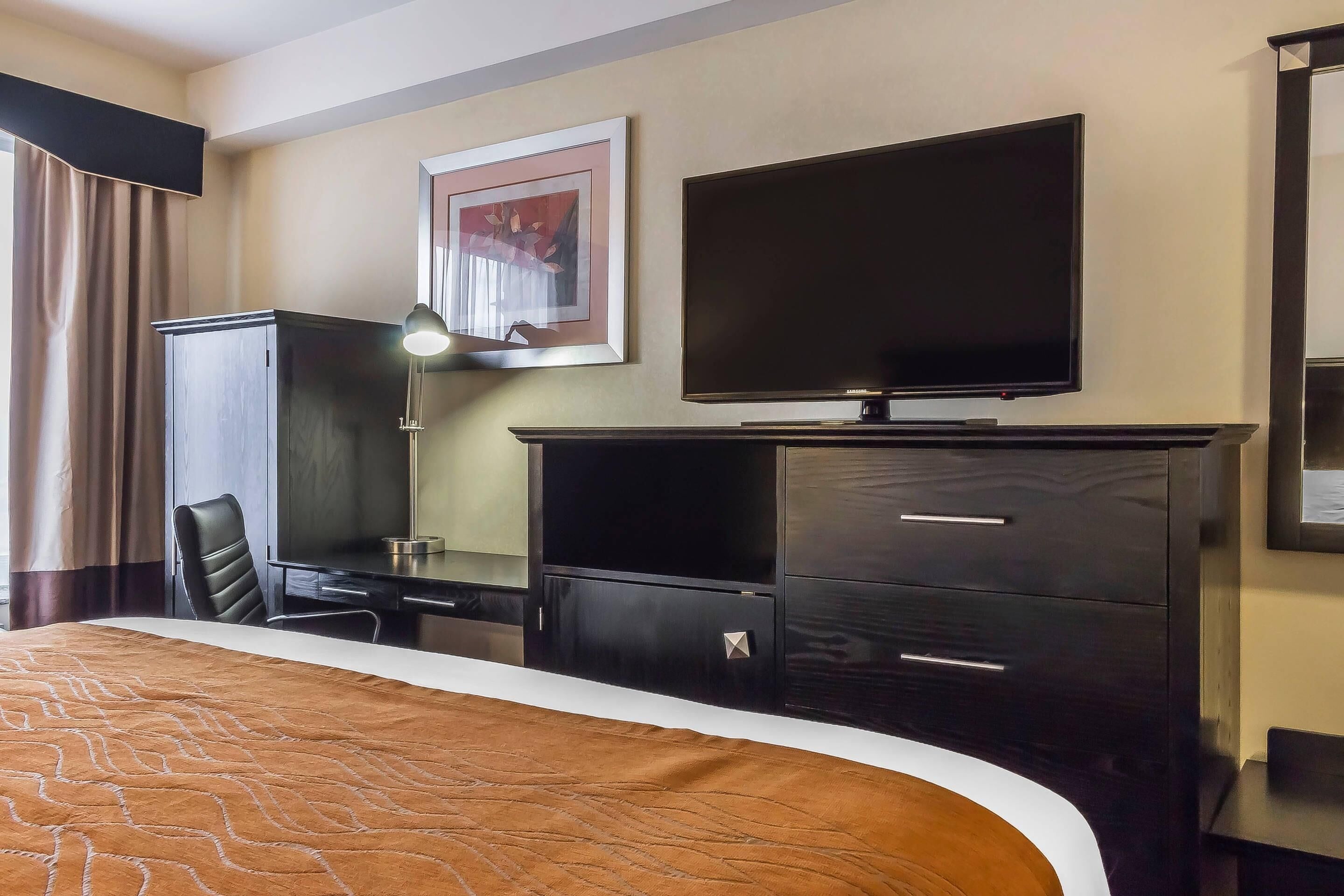 A hotel room with a bed, a desk, a chair, a television, and a wardrobe.