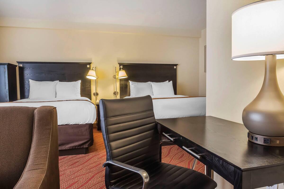 Hotellihuone, jossa on kaksi sänkyä, työpöytä, tuoli ja lamppu.