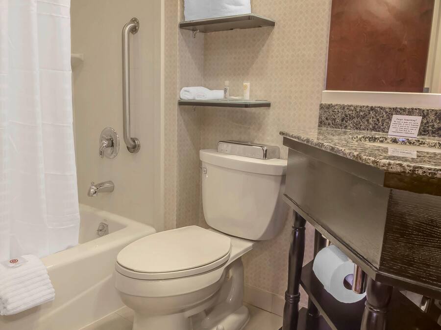 A bathroom with a bathtub, toilet, and a vanity with a sink. There are shelves above the toilet and a towel rack next to the bathtub.