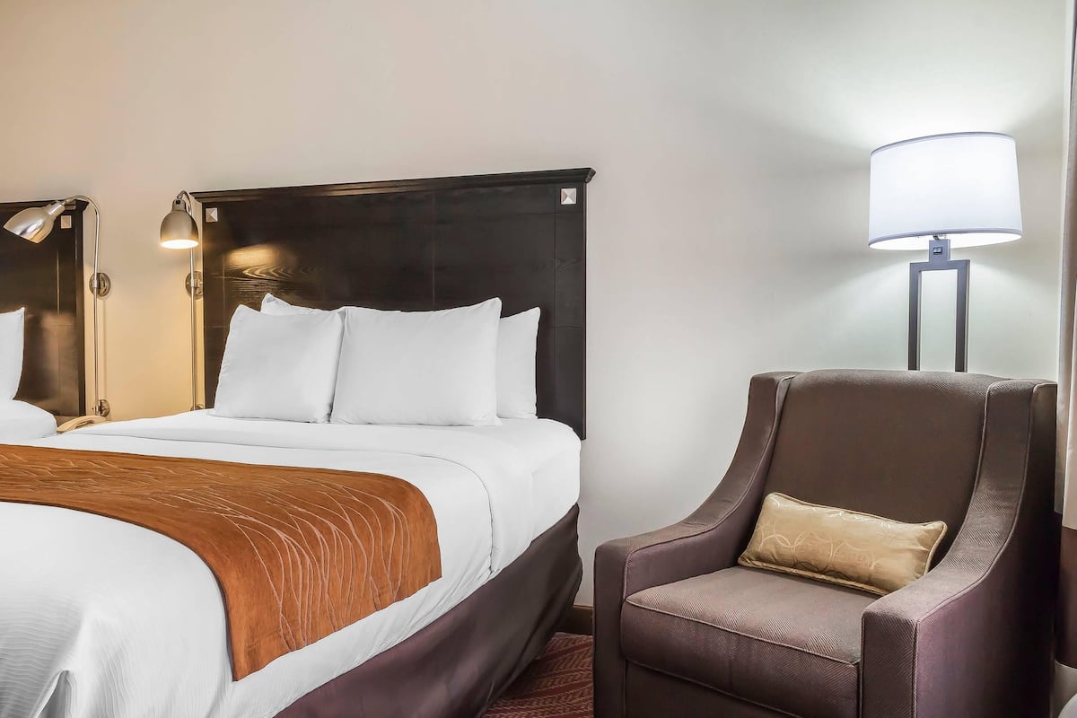 Hotellihuone, jossa on suuri sänky, tuoli ja kaksi yöpöytälamppua.