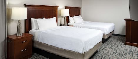 Habitación de hotel con dos camas, cabecera de madera, mesita de noche con lámpara y suelo alfombrado.