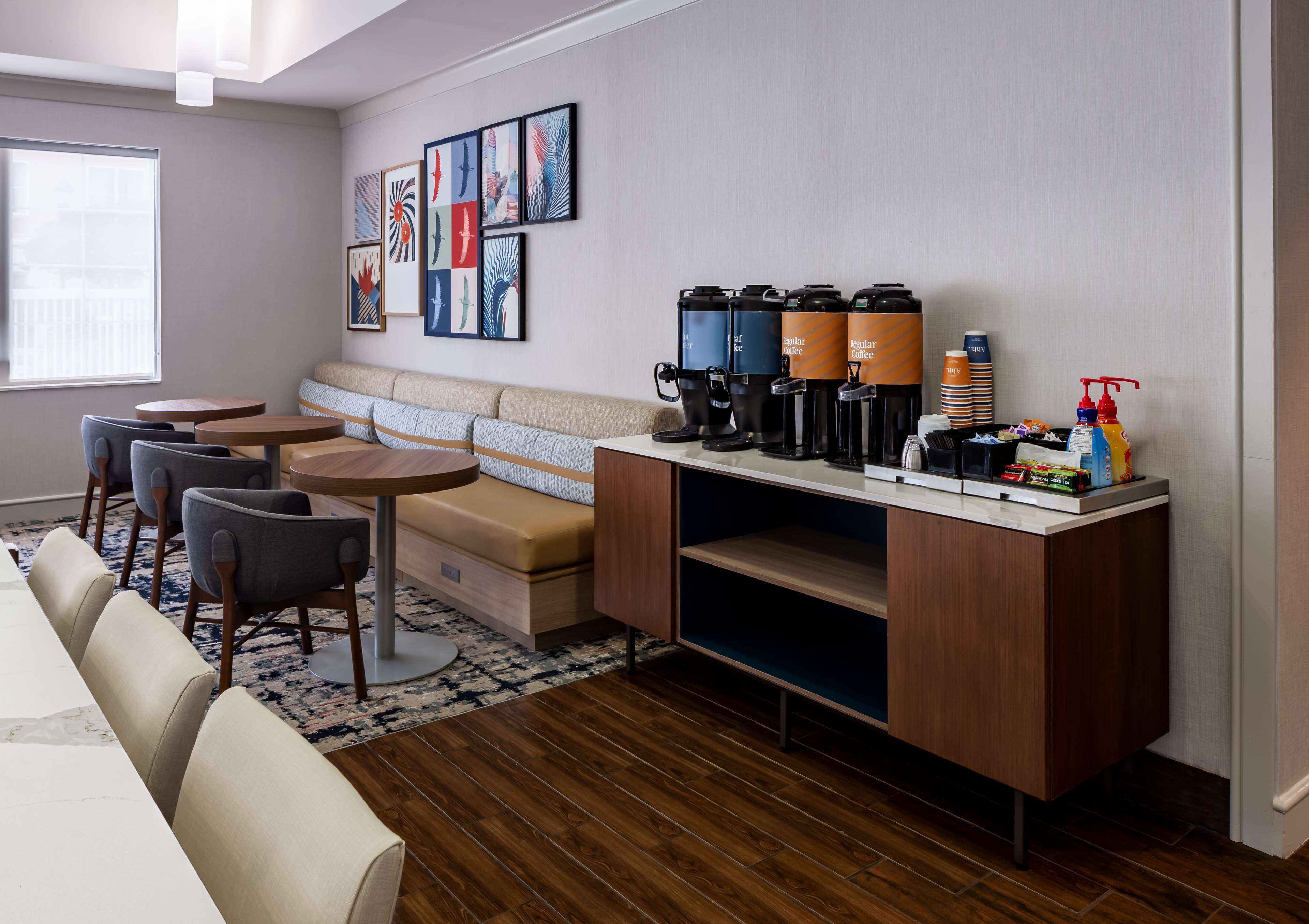 A modern hotel room with a sofa, two round tables, a coffee station, and artwork on the wall.