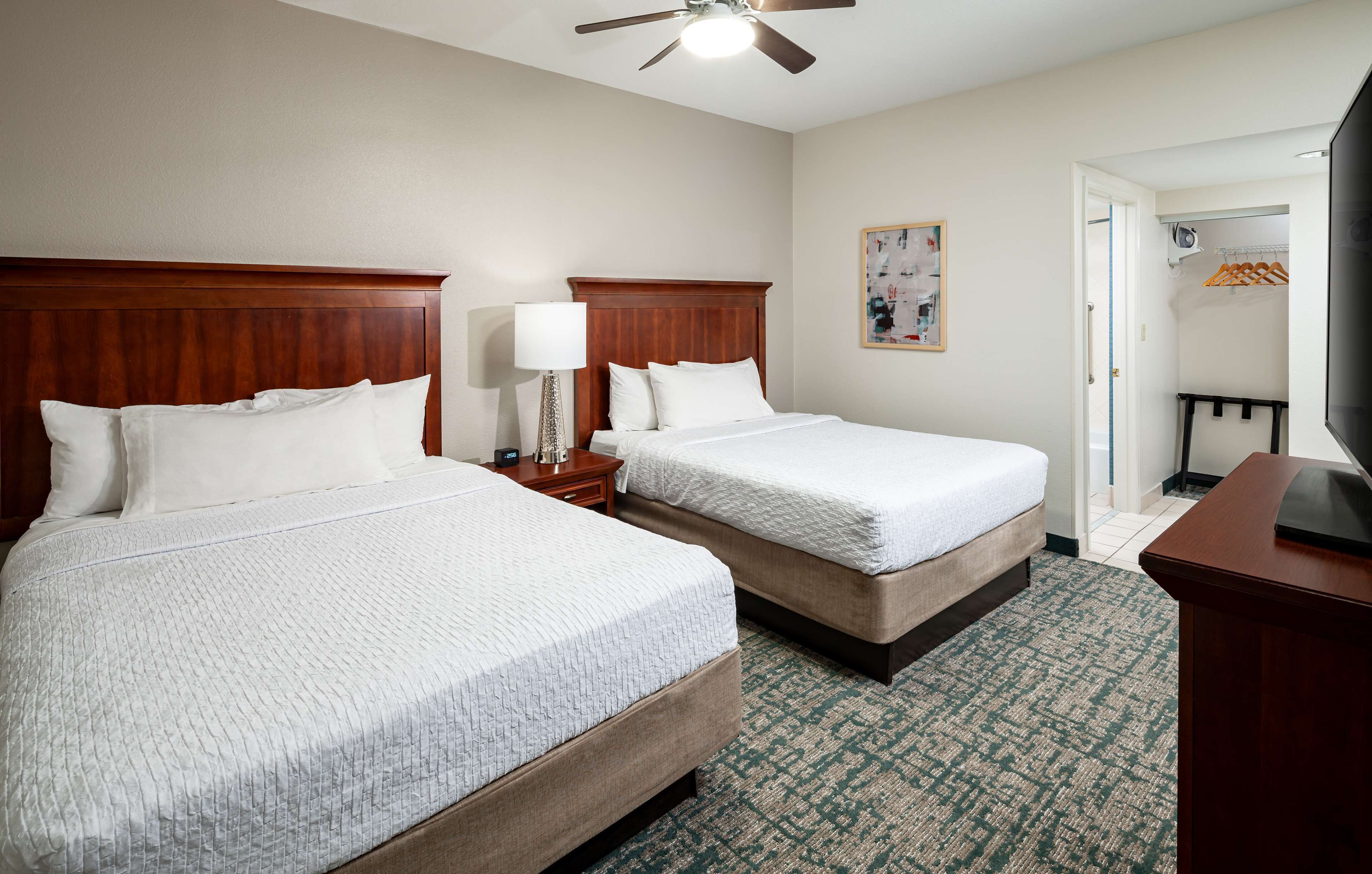 A hotel room with two beds, a ceiling fan, a TV, and a coat rack.