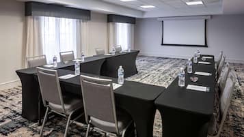 Uma sala de conferências com uma mesa comprida, cadeiras, garrafas de água e uma tela de projeção.