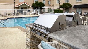 An outdoor pool area with a stone-tiled deck, a barbecue grill, and a lounge area with chairs and a table. - Homewood Suites by Hilton Jacksonville-South/St. Johns Ctr. (Jacksonville)