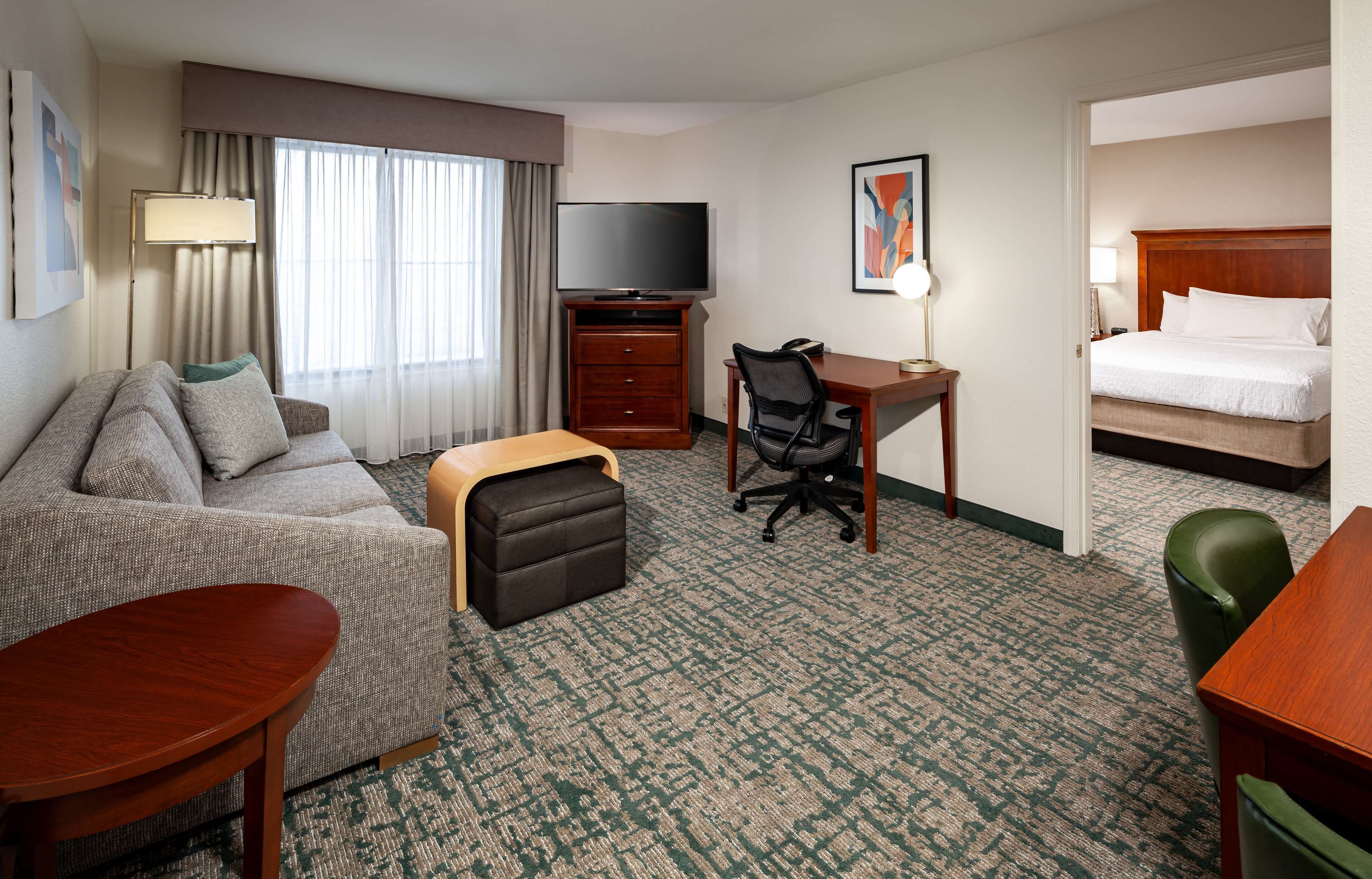 Una habitación de hotel con sofá, escritorio y silla, televisión, cama y piso alfombrado.