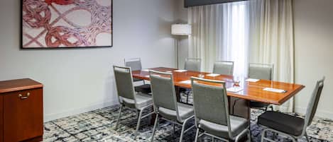 A conference room with a wooden table, four chairs, a cabinet, and a large abstract painting on the wall.