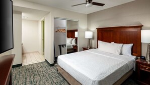 A hotel room with a large bed, a nightstand, a lamp, a TV, a closet, and a door leading to another room. - Homewood Suites by Hilton Jacksonville-South/St. Johns Ctr. (Jacksonville)