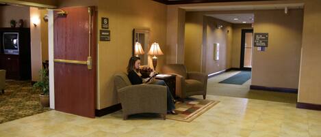 A lobby with a reception desk, a seating area with two armchairs, a red door, and a carpeted floor.