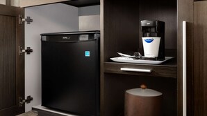 Una cocina compacta con un refrigerador negro, una cafetera y un cubo de basura.