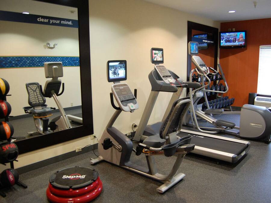 A gym with treadmills, elliptical machines, and a stepper. There are mirrors and a television on the wall.
