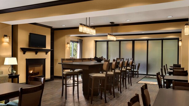 Un comedor de hotel con bar, varias mesas y sillas, una chimenea y un televisor en la pared.