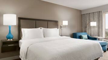 A hotel room with a large bed, a nightstand with a lamp, a chair, and a window with curtains.