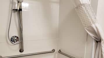Zona de ducha accesible, de color blanco, con ducha de mano, barras de apoyo y cortina de ducha blanca.