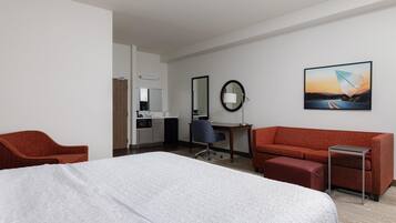 A hotel room with a large bed, a red sofa, a desk with a chair, a small table, and a painting on the wall.