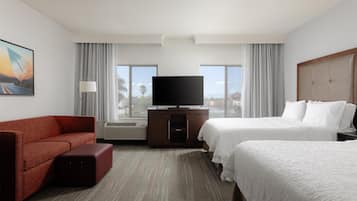 A hotel room with a red sofa, two beds, a TV, and large windows.